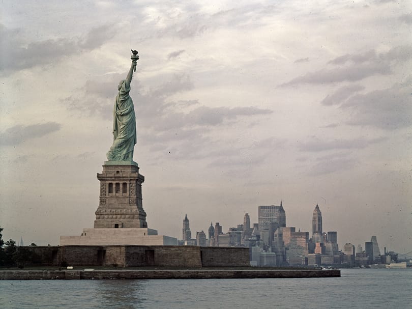 View of the Statue of Liberty from New York Harbor with the historic Lower Manhattan skyline visible in the background.