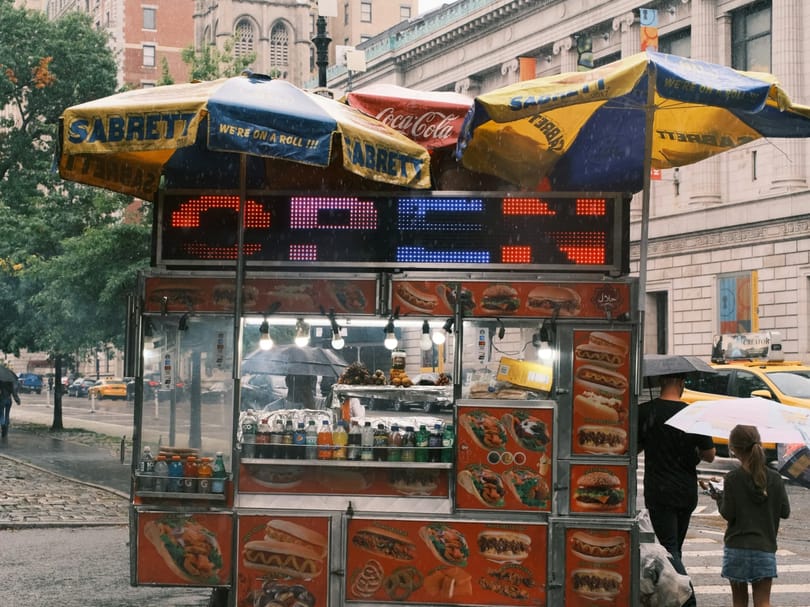 A food cart with umbrellas on a city street in NYC