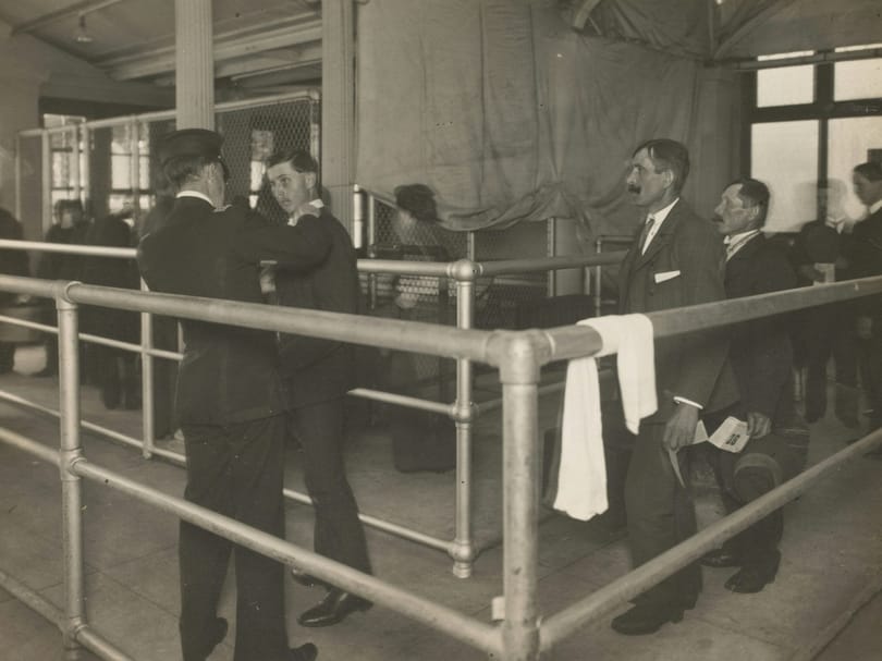 Greyscale image of men being medically inspected at Ellis Island